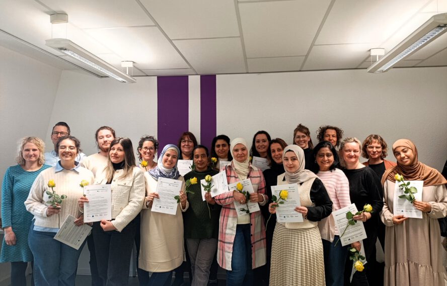 Ein Gruppenfoto der Absolvent:innen des Projektes "IQsA" des IQ-Netzwerks Bremen. Die Teilnehmenden halten ein ertifikat und eine gelbe Rose in der Hand. Copyright: Paritätisches Bildungswerk Bremen